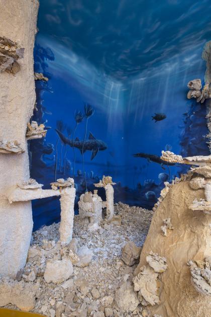 Ausschnitt vom Schauriff im Riffmuseum Gerstetten; Foto: Gemeinde Gerstetten Blick auf nachgebildete bleiche Felsriffe mit Korallen und Schwämmen. Im Hintergrund ist eine blaue Unterwasserwelt aufgemalt, mit urzeitlichen Pflanzen und Tieren.