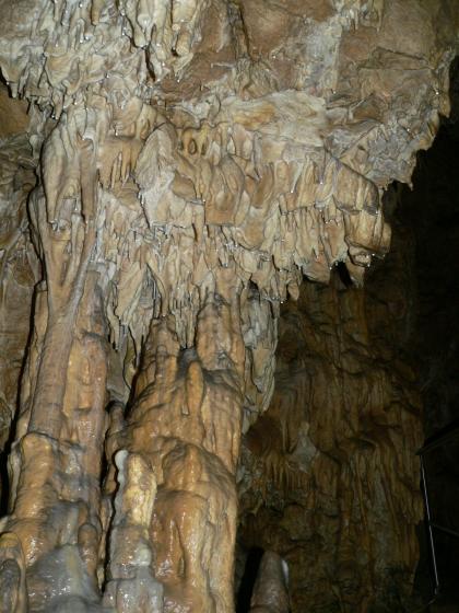 Kolbinger Höhle (Stephanshöhle), Kolbingen Blick auf graue und braune, von oben herunterhängende kleine Tropfsteine sowie dicke Säulen. Rechts im Hintergrund liegt eine Tropfsteinwand im Dunkel.