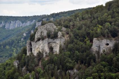 Blick vom Eichfelsen über das Donautal hinweg nach Nordosten zum Fachfelsen Blick auf mehrere große Felsformationen, die aus einem nach rechts ansteigenden, bewaldeten Berghang herausragen. Der größte Felsen, links der Bildmitte, hat eine kreisförmige Gestalt mit schroffen Wänden und oben einen gerundeten Block als Krone.