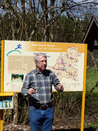 Vor einer orangefarbigen Schautafel, die das Thema „Abenteuer Natur auf der Zollernalb“ hat, steht, möglichen Besuchern zugewandt, ein Mann mit kariertem Hemd.