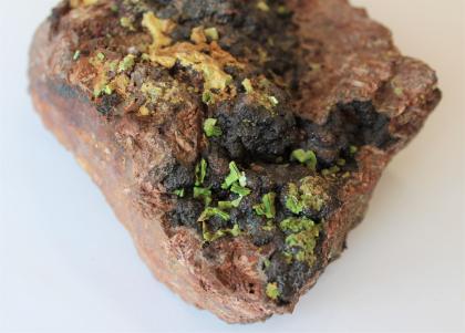Uranocitrit-Kristalle (gelb-grün) aus der Grube Krunkelbach bei Menzenschwand Großaufnahme eines unten dreieckigen Gesteinsstückes. Die rötlich braune Oberfläche weist schwarzgraue Knollen auf, an denen kleine grüne Kristalle sitzen.