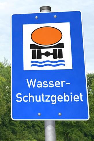 Wasserschutzgebiet: Hinweisschild Das Bild zeigt ein blaues Schild mit weißer Schrift, das auf ein Wasserschutzgebiet hinweist. Durch einen stilisierten Gefahrgut-Lkw wird außerdem zur besonderen Vorsicht gemahnt.