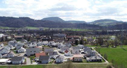 Von hoch oben blickt man auf eine weite Landschaft mit großen Waldflächen, Wiesen, Feldern und zahlreichen Siedlungen. Im Hintergrund erheben sich bewaldete Hügel und Berge.