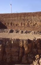 Ausschnitt aus einer braunen Steinbruchwand mit Abraumsohle in der Bildmitte. Unterhalb der Sohle sind größere Quader sichtbar, oberhalb verlaufen dünner gebankte Schichten.