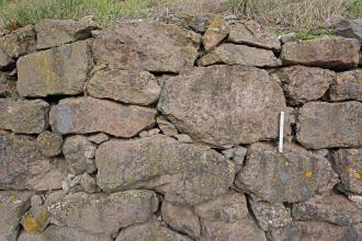 Detail einer Trockenmauer aus Brockentuff (Pyroklastit) entlang des geologischen Weinlehrpfads Achkarren Teilansicht einer grauen bis rötlich grauen Stützmauer, errichtet aus unregelmäßig geformten Gesteinsbrocken. Als Füllmaterial zwischen den Fugen dienen kleinere Steinchen.