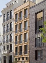 Das Bild zeigt die dreifach unterteilte Fassade eines mehrstöckigen Wohnhauses mit zahlreichen Fenstern. Die Fassaden bestehen aus grauem Klinker rechts sowie hellbraunen und weißen Steinplatten (mitte und links).