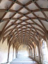 Blick in ein Kirchengewölbe mit hellem Putz und dunklen, sich überkreuzenden Stützbögen entlang der Decke.