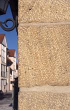 Nahaufnahme einer Hausecke aus hellbraunem, mit gelblichen Flecken durchsetztem Gestein.