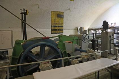 Fördermaschine im Silberbergwerk Teufelsgrund bei Münstertal Blick in einen Ausstellungsraum des Besucherbergwerks Teufelsgrund mit heller, gewölbter Decke. Im Vordergrund steht eine große Fördermaschine mit blaugrauem Schwungrad.