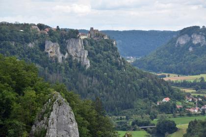 Blick vom Eichfelsen nach Nordosten durch das Obere Donautal mit seinen Felskränzen aus Schwammkalken des Oberjuras Blick aus großer Höhe auf einen nach links ansteigenden, bewaldeten Berg. An den Hängen des Berges treten graue Felsen hervor. Die Kuppe des Berges ist abgeflacht und teilweise bebaut. Rechts im Hintergrund steht ein weiterer Berg.