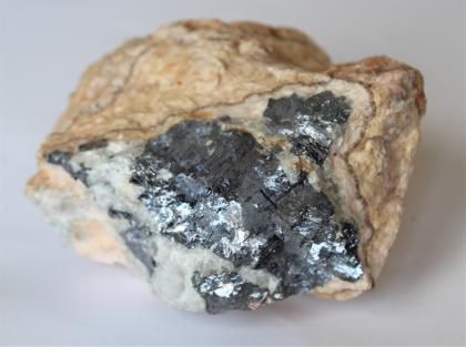 Galenit (bleigrau) aus dem Stollen Brenden im Mettmatal Handstück eines Gesteins, in Großaufnahme fotografiert. Die Vorderseite zeigt dunkelgraue und weißliche Stellen, während die Ränder und die Oberseite gelblich braun sind.