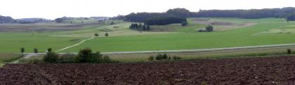 Kuppenalb bei Römerstein-Zainingen Panoramabild einer weiten, gewellten Landschaft mit Äckern und Grünflächen. Die Kuppen sind bewaldet. Im Vordergrund ist ein dunkelbrauner, erhöht liegender Ackerstreifen.