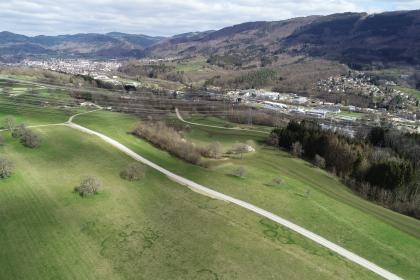 Blick vom Dinkelberg nach Nordosten ins Wehratal zwischen Wehr und Öflingen Blick aus der Luft auf welliges grünes Hügelland, durchzogen von Wegen und Hochspannungsleitungen. Rechts und im Hintergrund erheben sich bewaldete Berge. Davor breiten sich Siedlungen aus.