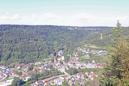 Blick über das Neckartal vom Weg oberhalb des Bollerfelsens auf Oberndorf am Neckar-Aistaig Blick aus großer Höhe auf bewaldete Berge sowie eine Siedlung, die im Vordergrund, am Fuß der Berge, liegt. Eine Bahnlinie durchschneidet den Ort. Rechts oben führt eine steile Bergstraße zu einer höher gelegenen Ortschaft.