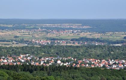 Blick vom Aussichtsturm Käpfle nach Nordnordwesten über die Härten zum Schönbuch Von erhöhtem Standort blickt man auf eine von Wald umschlossene Ortschaft. Dahinter folgt eine Ebene mit Wiesen und Feldern sowie weiteren Siedlungen und Waldflächen.