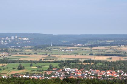 Blick über die Härten und das Neckartal östlich von Tübingen zum Schönbuch Von erhöhtem Standort schaut man auf eine weite Ebene mit Wiesen und Feldern, die sich am Fuße bewaldeter Berge ausbreiten. Im Vordergrund liegt eine Ortschaft an Waldrändern, links hinten ist eine größere Stadt erkennbar.
