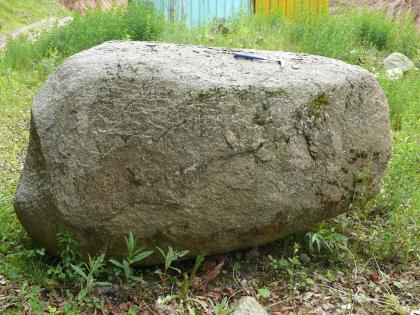 Durch Wollsackverwitterung gerundeter Granitblock Rundlicher, leicht länglicher Findling aus grauem Gestein auf einer Wiese.