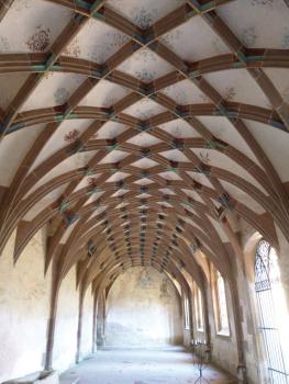 Netzgewölbe im Kloster Maulbronn aus gelblich braunem Schilfsandstein Blick in ein Kirchengewölbe mit hellem Putz und dunklen, sich überkreuzenden Stützbögen entlang der Decke.