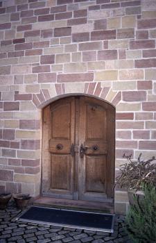 Farbvarietäten des Württembergischen Schilfsandsteins bei einem Möbelhaus in Stuttgart-Plieningen Blick auf eine Gebäudewand aus mehrfarbigen Mauersteinen. Eine Doppeltür aus Holz bildet den Eingang.