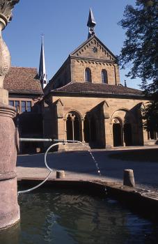Das vollständig aus Schilfsandstein erbaute Zisterzienserkloster von Maulbronn Blick auf ein Klostergebäude aus hellbraunem Mauerwerk mit Eingangshalle und spitzem Eckturm. Im Vordergrund ein Steinbrunnen.