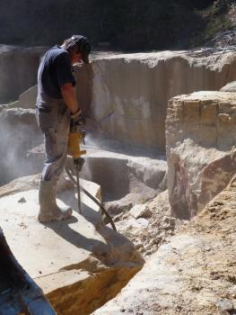 Abbau im Stubensandsteinbruch Pliezhausen-Rübgarten Blick auf einen Arbeiter in einem Steinbruch, der – auf einem Steinblock stehend – diesen mit einem Bohrgerät bearbeitet. Im Hintergrund Steinbruchwände.