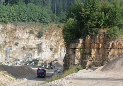 Nordteil des Steinbruchs Tuttlingen-Eichen Blick in einen Steinbruch von der Zufahrt aus, mit halbhohen Bruchwänden rechts vorne und hohen Wänden links im Hintergrund. Vor der hinteren Wand sind Fördergeräte aufgestellt. Die Kuppen der Bruchwände sind bewaldet.