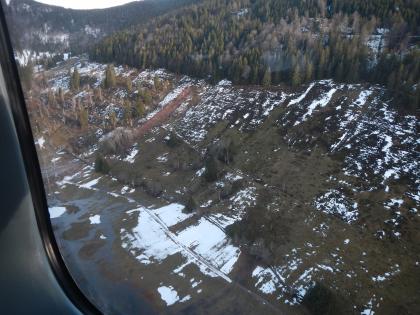 Neu entstandene Hangmure am Hang ca. 700 m nördlich von Menzenschwand-Hinterdorf (Aufnahme aus Polizeihubschrauber) Man blickt aus dem Fenster eines Hubschraubers auf einen oben bewaldeten, aber sonst recht kahlen Hang. Im Zentrum des Bildes ist am Hang deutlich eine Hangmure zu erkennen, die sich über eine Straße erstreckt.