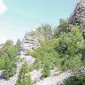 Blick auf einen nach rechts steil aufsteigenden Felshang mit hellem Gestein. Links der Bildmitte erhebt sich eine oben abgerundete Felsnadel. Im unteren Hangteil liegt Blockschutt. Dazwischen wachsen Bäume und Büsche.