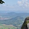 Blick aus großer Höhe auf Felder und bewaldete Berge. Links sind mehrere Ortschaften verteilt. Rechts vorne ist ein vorspringender Felsenkopf ganz nahe. Im dunstigen Hintergrund verläuft ein Höhenzug mit drei markanten Erhebungen.