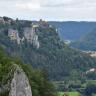 Blick aus großer Höhe auf einen nach links ansteigenden, bewaldeten Berg. An den Hängen des Berges treten graue Felsen hervor. Die Kuppe des Berges ist abgeflacht und teilweise bebaut. Rechts im Hintergrund steht ein weiterer Berg.