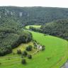 Blick aus großer Höhe auf eine Schlinge der Donau. Der Fluss verläuft von rechts unten zur Bildmitte hin und verschwindet dort zwischen bewaldeten Bergen. Das linke Ufer ist flach, daran schließen sich bewaldete Berge an, die bis zum Hintergrund reichen. 
