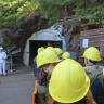 Das Bild zeigt eine Besuchergruppe des ehemaligen Bergwerks Finstergrund mit gelben Schutzhelmen. Der Eingang zum Bergwerk liegt in der Mitte des Bildhintergrunds.
