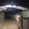 Blick auf einen breiten, niedrigen Tunnel mit zwei Spurbahnen für Förderwagen im Besucherbergwerk Finstergrund. Die nur im Vordergrund von einer Lampe beleuchteten Wagen auf der Spur rechts sind mit Abbaumaterial beladen. Die linke Spur ist frei.