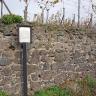 Leicht seitlicher Blick auf eine aus dunkelgrauen (unten) bis hellgrauen Steinbrocken aufgeschichtete Stützmauer. Die verfugte Mauer an einem Rebhang ist Station des geologischen Weinlehrpfads in Achkarren. 