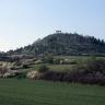 Oberhalb einer gewölbten, mit Bäumen und Büschen gesäumten grünen Landschaft erhebt sich ein grüner, von Bäumen bestandener Berg. Auf dessen Kuppe steht eine Kapelle. Der Bildvordergrund ist ebenfalls grün, aber flach.
