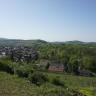 Blick von erhöhtem Standort über eine weite Landschaft mit Wald, bewaldeten Bergen sowie einer Ortschaft links und im Mittelgrund. Im Vordergrund links befindet sich ein Wiesenhang mit Legesteinen, rechts sind Rebanlagen sichtbar.
