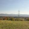 Blick auf hochgelegene Wiesen mit Baumbestand im Mittelgrund. Am Horizont verlaufen bewaldete Bergrücken.
