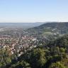 Von sehr hohem Standort blickt man über eine größere Stadt links und bewaldete Bergrücken rechts.