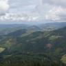 Blick aus großer Höhe auf zahlreiche bewaldete Berge. An Hängen und tieferen Stellen finden sich baumlose Flächen mit einzelnen Häusern. Links hinten ist auch eine größere Siedlung erkennbar.