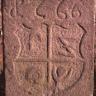 Blick auf einen hohen, aus rötlich grauem Stein gefertigten Grenzstein mit eingeprägtem Wappen und Jahreszahl.