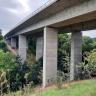 Blick auf eine hohe und breite Betonbrücke. Die Brücke wird von einer Doppelreihe Pfeilern gestützt und überwindet einen V-förmigen, mit Bäumen bestandenen Geländeeinschnitt.
