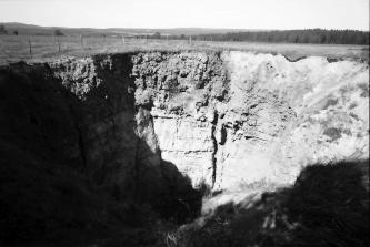 Altes Schwarzweißfoto, das den tiefen Krater einer Doline zeigt. Gestein und Bodenmaterial sind auf einer hochgelegenen Wiese eingestürzt.