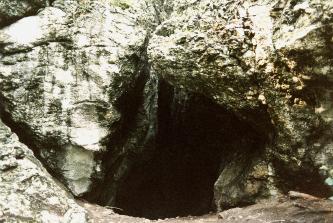 Blick auf den von keilförmigem Gestein gesäumten Eingang zu einer Höhle. Im hellgrauen Felsgestein über und neben der Höhle verläuft links vom Boden aus ein schräg ansteigender Riss.