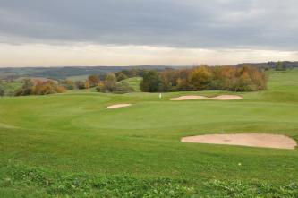 Das Bild zeigt einen hügeligen, grünen Golfplatz. Auch einzelne Sandinseln und Baumgruppen sind zu sehen.