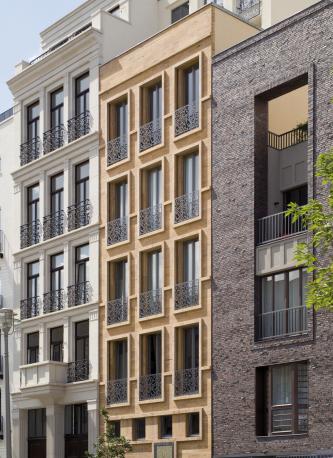 Das Bild zeigt die dreifach unterteilte Fassade eines mehrstöckigen Wohnhauses mit zahlreichen Fenstern. Die Fassaden bestehen aus grauem Klinker rechts sowie hellbraunen und weißen Steinplatten (mitte und links).