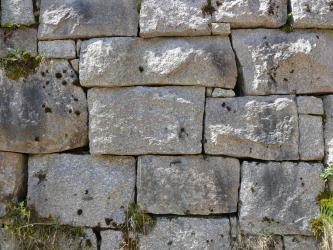 Das Bild zeigt eine Trockenmauer aus rechteckigen, hellgrauen Gesteinsblöcken. Die Blöcke haben alle eine leicht unterschiedliche Form. Manche Mauerfugen sind bewachsen.