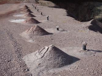 Bohrlöcher mit grauer Verrohrung entlang einer Steinbruchkante mit Haufwerken aus feinkörnigem Gesteinsmehl.