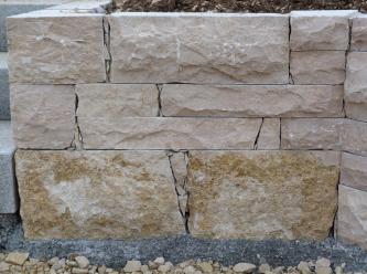 Teilansicht einer Steinmauer. Der untere Teil zeigt grünlich braune Quader, darüber sind die Steine rötlich grau. Breite Fugen zwischen den Steinen sind mit kleinen Bruchstücken gefüllt.